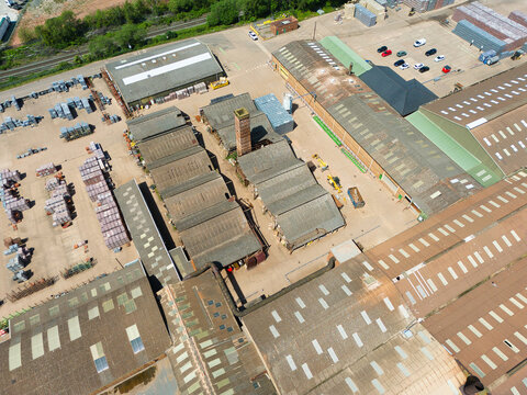 Aerial view of Kingsbury Brick Works and Factory featuring large industrial warehouses, a tall brick chimney, and stacks of building materials in Dosthill, England, United Kingdom.