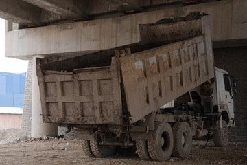 Fototapeta premium Dirty dump truck with its bed raised under a concrete bridge