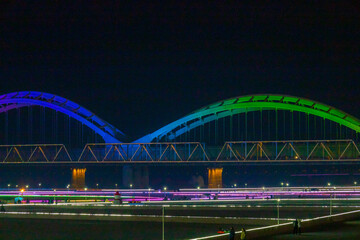 Fototapeta premium Night view of an illuminated city bridge over river with skyline and water reflections in Harbin, China.