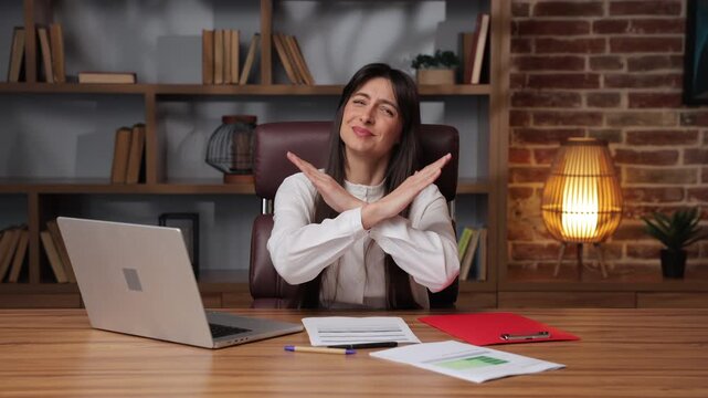 Business woman smiles and makes stop gesture at office desk during work hours.