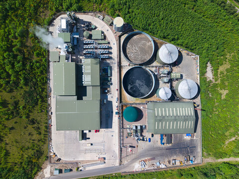Aerial view of Biogen Atherstone anaerobic digestion plant with circular storage tanks and industrial buildings surrounded by green forest in Atherstone, England, United Kingdom.