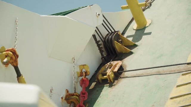 Closeup mooring gear on deck, cinematic k drone capture showing anchor chain wrapped around capstan and bollard, weathered green paint, rust stains, yellow safety post, strong sunlight and sharp