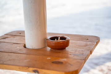 Wooden beach table with ashtray stands beside a sun umbrella at a resort in Sharm El Sheikh Egypt with sandy background. Beach relaxation and resort lifestyle © timoha.ig