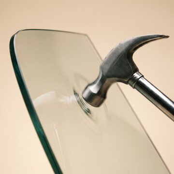Metal hammer striking tempered safety glass sheet demonstrating impact resistance