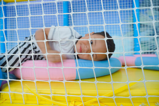 Child lies on colorful play mat inside safety net. Smiling face shows happy, relaxed emotion