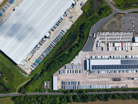 Aerial view of large industrial warehouses with rows of parked semi-trailers and solar panels on the roof in Hinckley, England, United Kingdom.