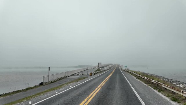 Driver&rsquo;s perspective on the road leading to Assateague Island, Maryland, with dense fog surrounding both sides of the roadway and obscuring the distant coastal landscape