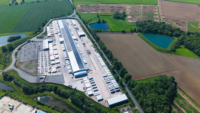 Aerial view of a large distribution center with solar panels on the roof and semi-trailers parked in bays surrounded by green fields Hinckley, England, United Kingdom.