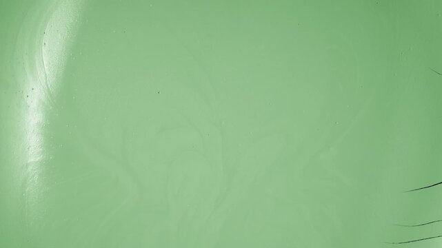 Top angle time-lapse shot of a flat pale green surface drying, forming visible cracks and a fragmented texture resembling natural mudcracks
