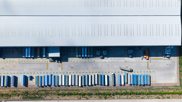 Aerial view of a large distribution center with rows of semi-trailers parked at loading docks under bright sunlight Hinckley, England, United Kingdom.