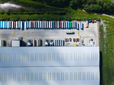 Aerial view of a large logistics warehouse with rows of colorful semi-trailers parked at loading docks next to a corrugated metal roof Hinckley, England, United Kingdom.