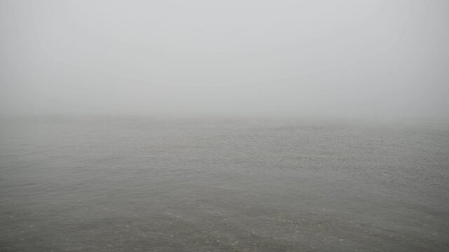 A calm inland lake at Assateague Island enveloped in dense fog, with still water blending into the mist and obscuring the distant shoreline, creating a quiet and atmospheric coastal wetland scene