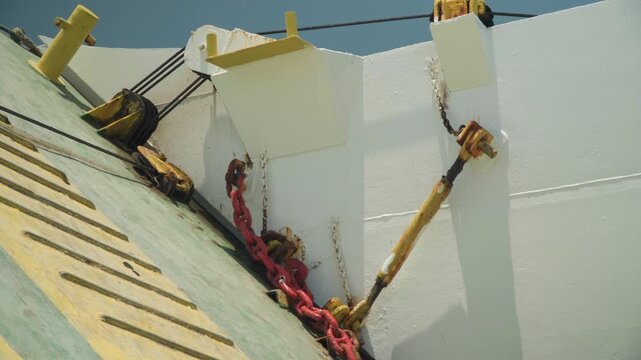 White hull with red chain, angled view of bollard, winch and mooring line bright sunlight, clean paint, diagonal composition and coastal port setting suggesting rigging technician work, dock