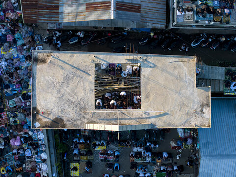Aerial view of people gathered on prayer mats for Eid Al-Adha prayer between rooftops and urban structures in Kecamatan Kalikajar, Jawa Tengah, Indonesia.
