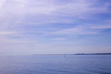Calm sea horizon with distant sailboat under soft clouds and blue sky creating a peaceful maritime landscape. © Iryna Miadzvedzeva