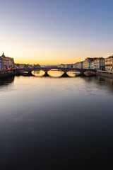 Obraz premium The Ponte Santa Trinita bridge spans the Arno River in Florence, Italy, during a beautiful sunset with clear skies.