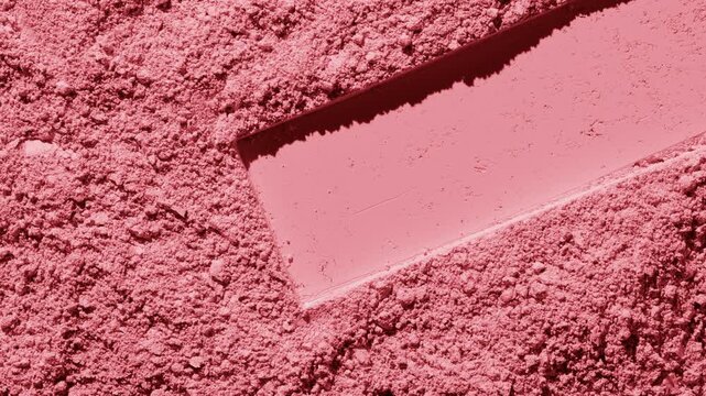 Overhead capture of red natural powder surface imprinted with a stretched rectangular shape lit with orbiting directional light casting dynamic shadows