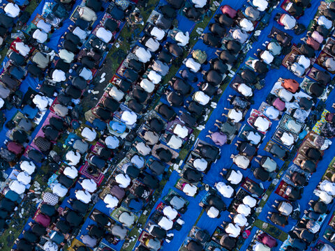 Aerial view of a large crowd of Muslim worshippers performing Eid Al-Adha prayer in Garung on colorful mats and blue tarps Kecamatan Kalikajar, Jawa Tengah, Indonesia.