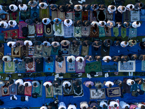 Aerial view of Muslim men performing Eid Al-Adha prayer on colorful prayer rugs and blue tarps in Kecamatan Kalikajar, Jawa Tengah, Indonesia.