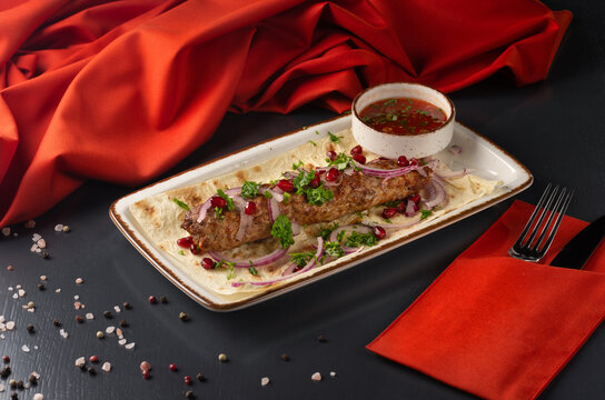 Grilled Lula kebab on skewers with spices in a black plate on a dark background.