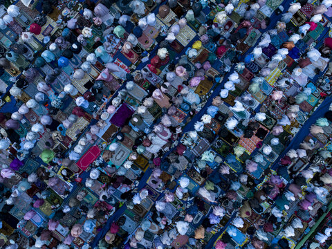 Aerial view of people gathered for Eid Al-Adha prayer on colorful prayer mats creating a vibrant pattern of rows and textiles Kecamatan Kalikajar, Jawa Tengah, Indonesia.