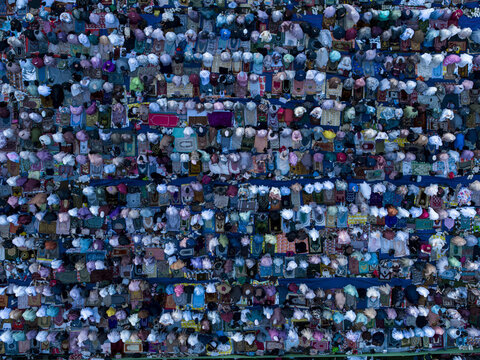 Aerial view of a large crowd of people gathered for Eid Al-Adha prayer on colorful prayer mats in Kecamatan Kalikajar, Jawa Tengah, Indonesia.