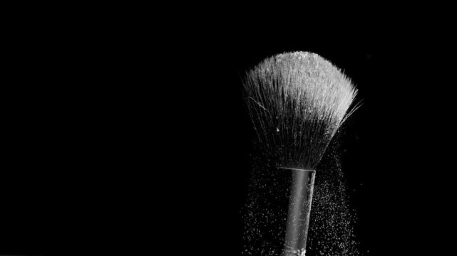 Slow-motion macro shot of black brush flicking white powder against a black backdrop | Setting powder promotional concept