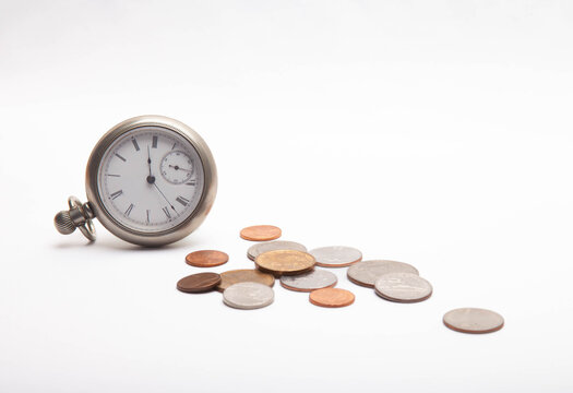 Vintage pocket watch beside scattered coins on a clean white surface conveys time, money, savings and financial planning concepts, suggesting investment, budgeting, economy and the value of time.