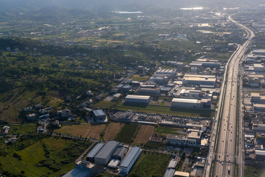 Aerial view of industrial warehouses and commercial buildings along a major highway stretching towards distant hills in Tirana County, Albania.