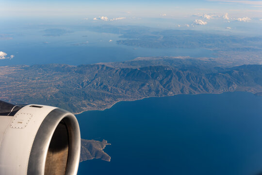 Aerial view of the Aegean Sea coastline featuring rugged mountains and an airplane engine in the foreground under a clear blue sky Greece.