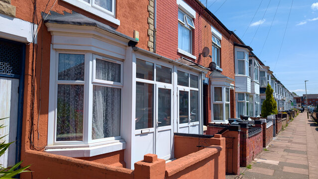 Terraced houses in UK, British suburban street with red brick residential buildings, row of typical English homes on sunny day, real estate neighborhood background
