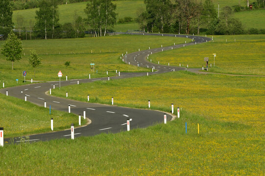 Empty winding road through green spring meadows in the rural countryside of Styria, Austria