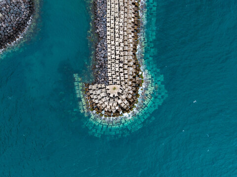 Aerial view of the geometric concrete breakwater and tetrapods surrounded by deep blue turquoise water at the harbor in Povoacao, Acores, Portugal.