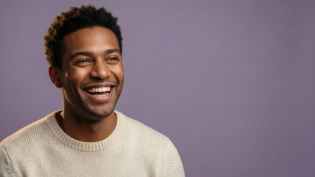 Portrait d'un jeune homme afro-am&eacute;ricain heureux au sourire &eacute;clatant, portant un pull couleur cr&egrave;me sur fond studio violet uni, regardant sur le c&ocirc;t&eacute; avec une expression joyeuse