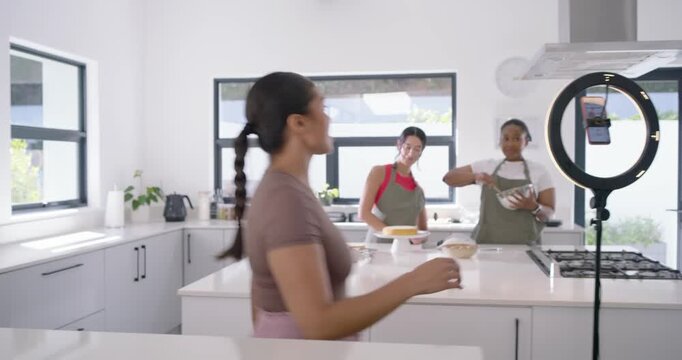 Three women moving after ring light cue placing phone rig filming cake in kitchen for demo