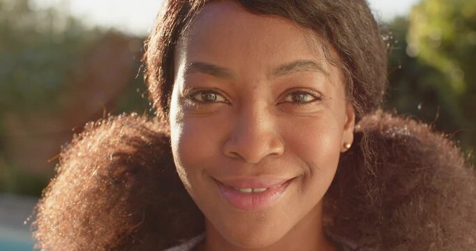 Adult African woman meeting camera gaze smiling laughing under golden garden light with studs puffs