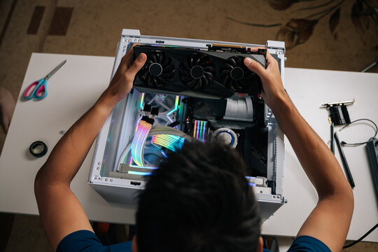 High-angle view of computer technician carefully inserting high-performance graphic card inside gaming desktop, upgrading powerful system with vibrant RGB lighting for maximum computing potential