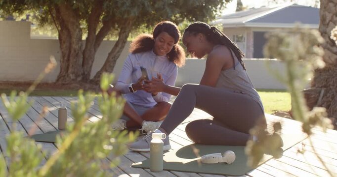 African women sharing phone clip and pointing at screen reviewing progress on deck with yoga mats