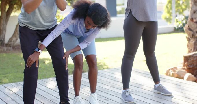 African American trio squatting on deck, center woman checking left man's knee for form, smartwatch