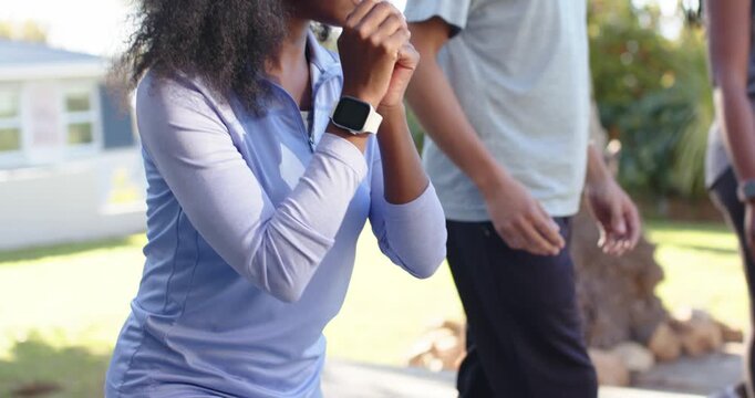 Friends following leader, doing synced squats in sportswear on patio by palm tree, wearing watches