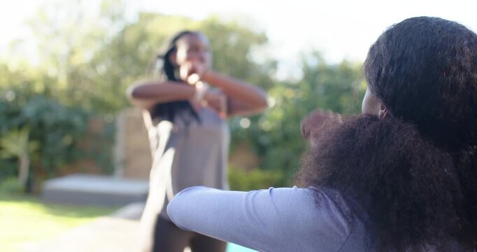 Two African American women following smartwatch beep, doing synchronized arm-cross warm-up by pool