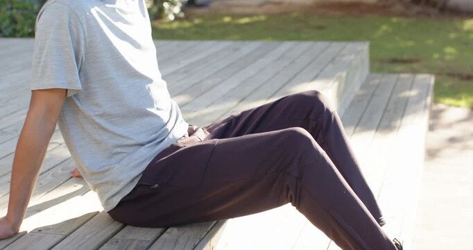 Camera pulling back, African American man sitting on wooden steps in black sneakers and reflecting