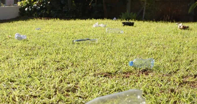 Camera pulling back is revealing crushed bottle and litter across sunny yard, showing extent