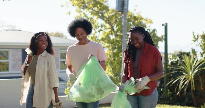 Volunteers walking front yard during cleanup, wearing gloves, using picker, filling green bags