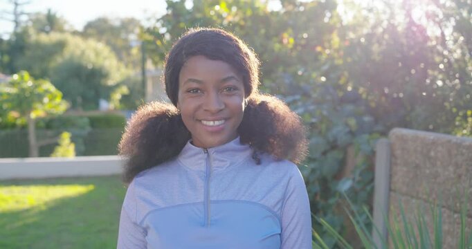 Adult woman smiling wider as sunlight flaring behind, tilting head, showing light-blue zip pullover