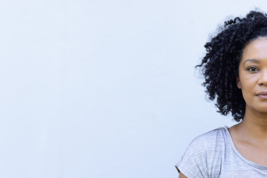 African American woman posing against pale blue-gray wall in studio, wearing gray top, copy space