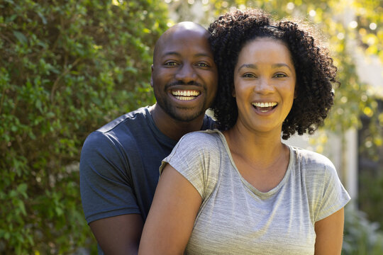 African American couple posing among sunlit foliage smiling, man embracing woman, wearing grey tees