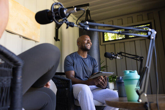 African man and female speaking into boom mics, holding tablet in small studio with punching bag