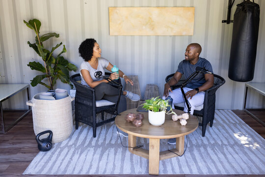 African American co-hosts in sportswear speaking into broadcast mics on boom arms in studio gym