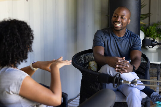 African man and woman sitting on porch recording with boom microphones, man wearing gray sweats